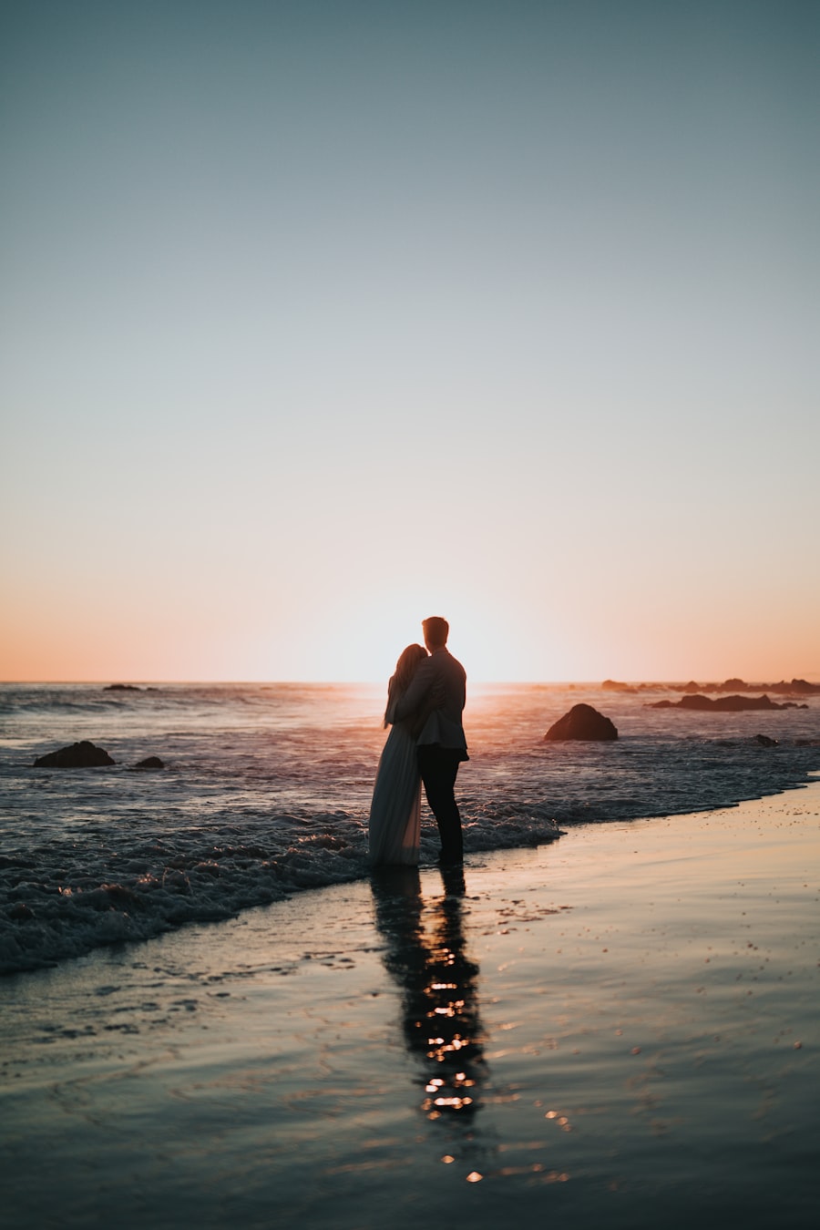 Silhouette of a couple embracing at the ocean's edge at sunset